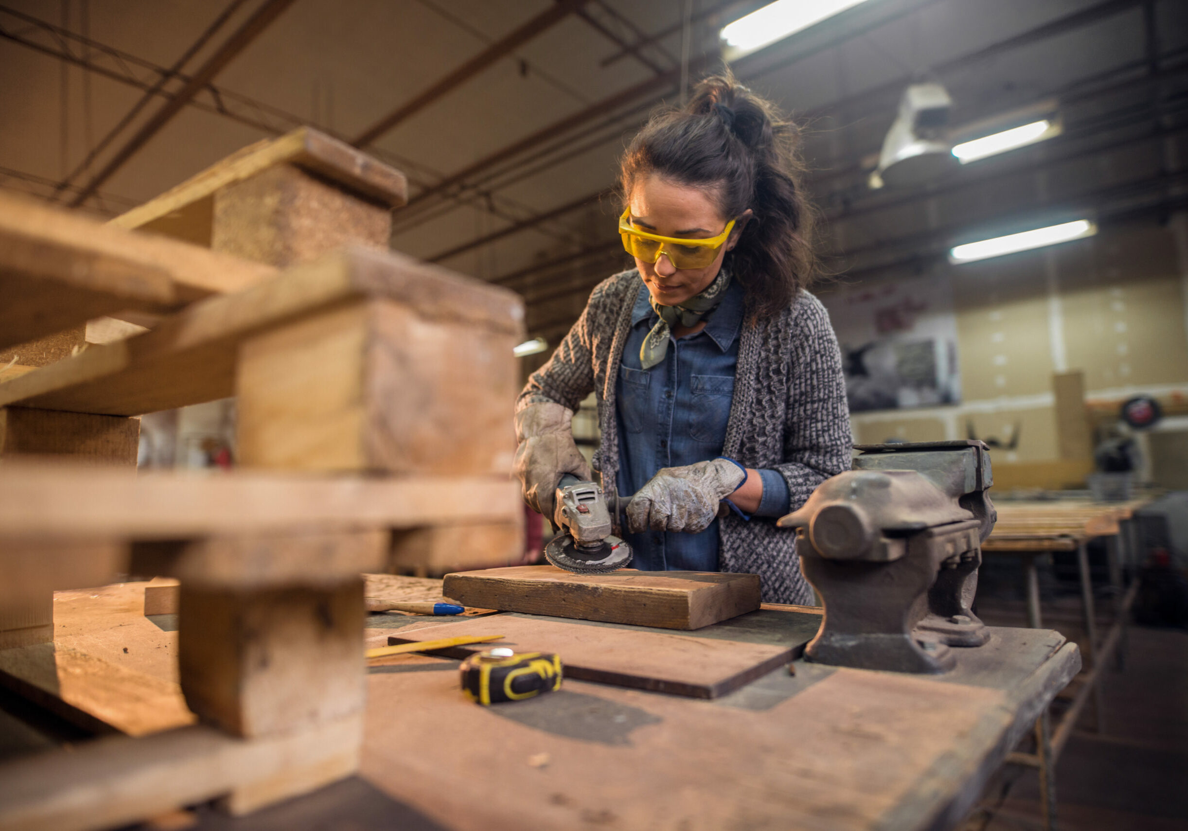 Female carpenter working with sander while standing surrounded with wood.